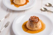 From above of egg custards topped with sweet Dulce de leche served on white plates on table with cutlery in kitchen — Stock Photo