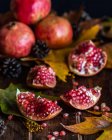 Partes de romã vermelha fresca colocadas sobre mesa de madeira escura com folhas de outono — Fotografia de Stock