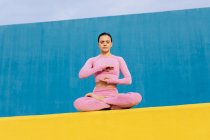 Femme calme et flexible assise à Padmasana et méditant les yeux fermés tout en pratiquant le yoga sur fond bleu et jaune vif — Photo de stock