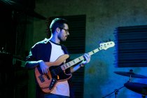 Grave giovane che suona il basso mentre si esibisce in un club leggero con illuminazione al neon — Foto stock