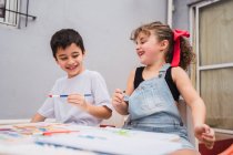 Позитивные дети с кистями живописи с красочными акварелями на бумаге за столом — стоковое фото