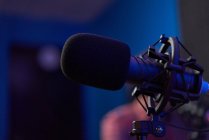 Microphone moderne sur trépied placé sur la table dans un studio sombre avec éclairage au néon avant l'enregistrement podcast — Photo de stock