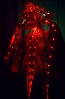 Нерозпізнавана загадкова жінка у творчому традиційному одязі та в'єтнамському головному уборі з червоним освітленням, що стоїть у темній студії на чорному тлі під час виступу. — стокове фото