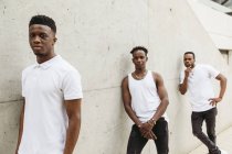 Coole afroamerikanische Freunde in trendiger Kleidung mit weißem T-Shirt stehen in der Nähe des Gebäudes und schauen in die Kamera — Stockfoto