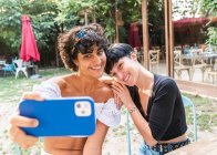 Contenus femmes multiraciales amicales prenant auto tiré sur le téléphone mobile tout en profitant week-end ensemble dans le parc d'été — Photo de stock