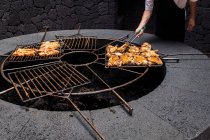 Crop anonymous male grilling delicious chicken pieces on rack above volcano heat in Natural Park of Timanfaya in Lanzarote Spain — Stock Photo