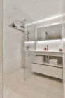 Bagno moderno interno con lavabo e specchio contro la doccia con parete di vetro in casa luce — Foto stock