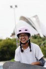 Giovane donna afroamericana sorridente in occhiali con casco protettivo lilla chiaro e gomitiere grigie che pattinano nel parco — Foto stock