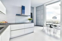 Design criativo de cozinha e sala de jantar com lâmpada e mesa contra janela em casa de luz — Fotografia de Stock