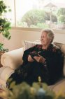 Зосереджена старша жінка з сірим волоссям відпочиває на дивані і читає електронну книгу на планшеті у вітальні вдома — стокове фото