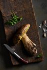 Top view of raw cut Boletus edulis mushrooms on wooden chopping board with garlic and parsley in light kitchen during cooking process — Stock Photo
