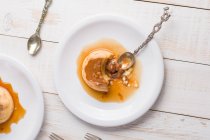 Vista superior de creme de ovo fresco coberto com doce dulce de leche servido com xarope em mesa de madeira com talheres na cozinha — Fotografia de Stock