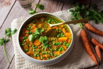 Schüssel mit köstlichem Carry Mahlzeit mit Gemüse garniert mit grünem Basilikum Blätter serviert in der Nähe Topf auf dem Tisch mit rohen Karotten — Stockfoto