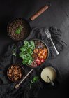 Top view of stewpan with lentils near salad with pumpkin and bell pepper decorated with green basil leaves on black background near salad dressing — Stock Photo