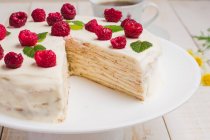 Sabroso pastel de crema keto saludable con edulcorante eritritol decorado con frambuesas maduras servidas en mesa de madera con ramitas decorativas en la cocina - foto de stock