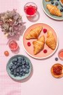 Зверху композиція покрита свіжими запеченими солодкими круасанами, які подаються з ягодами та варенням, поміщеними на рожевий стіл — стокове фото