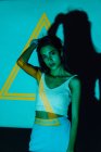 Fresco giovane femmina etnica in crop top guardando la fotocamera contro triangolo giallo e ombra — Foto stock
