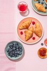 Зверху композиція покрита свіжими запеченими солодкими круасанами, які подаються з ягодами та варенням, поміщеними на рожевий стіл — стокове фото