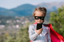 Самозабезпечена дівчина в костюмі супергеройської маски з мисом, що переглядає мобільний телефон — стокове фото