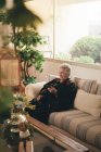 Focado sênior feminino com cabelos grisalhos descansando no sofá e lendo e livro em tablet na sala de estar em casa — Fotografia de Stock