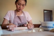 From below woman in apron rolling dough on table while preparing dumplings with meat in kitchen — Stock Photo