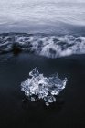 Desde arriba de trozo de hielo brillante en la playa de arena negra lavado por el océano ondulado en el día nublado en Islandia - foto de stock
