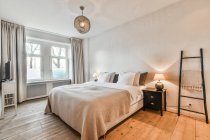 Ліжко з кришкою і подушками під лампою, що висить на вікні вдома з дерев'яною підлогою — стокове фото