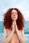 Mulher pacífica de pé com os olhos fechados na praia e fazendo gesto namaste durante a meditação — Fotografia de Stock