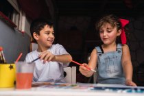 Позитивні діти з фарбувальними пензлями з барвистими акварелями на папері за столом — стокове фото