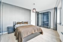 Сучасний інтер'єр спальні з подушками і покриттям на ліжку проти столу і шафи на підлозі в легкому будинку — стокове фото