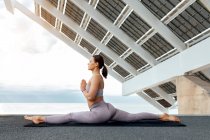 Full body of peaceful female practicing front splits forward bend asana on street with solar panel in city — Stock Photo