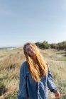 Glückliche junge Frau in lässigem Outfit steht im Sommer auf der Wiese und blickt in die Kamera — Stockfoto