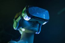 Frauenattrappe in futuristischer VR-Brille unter heller Projektion in schummrigem Raum platziert — Stockfoto