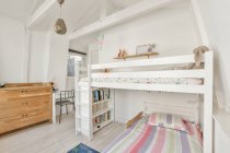 Litera blanca con estanterías y alfombra de colores cerca de la puerta en la luz dormitorio moderno de los niños - foto de stock