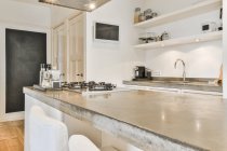 Design creativo della cucina con bottiglie sul tavolo contro lavello e TV a parete in casa luce — Foto stock