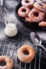 Сладкие жареные пончики подаются на тарелке возле металлической стойки охлаждения и кувшин молока на черном грязном столе с сахарной пудрой — стоковое фото