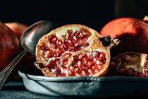 Halbierter und ganzer reifer Granatapfel auf Bratpfanne auf faltiger Tischdecke auf dem Tisch — Stockfoto