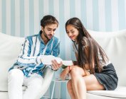 Uomo e donna sorridente seduta su poltrone bianche e guardando brochure in salone — Foto stock