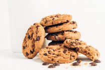 Pile of sweet crunchy cookies with chocolate chips placed on table with crumbs and milk on white background in room — Stock Photo