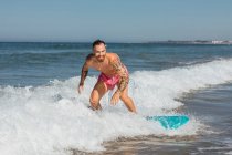 Homme actif en short de natation debout sur une planche de surf tout en surfant en mer dans une station tropicale lors d'une journée ensoleillée d'été — Photo de stock