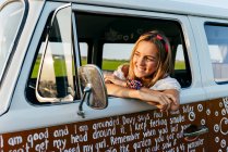 Carina ragazza bionda seduta all'interno di un furgone vintage e appoggiata alla finestra in una giornata di sole — Foto stock