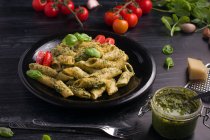 From above of plate with delicious pasta with green pesto sauce and tomatoes served on black wooden table — Stock Photo