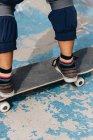 Anonyme junge ethnische Person in lässigem Outfit mit schützenden Knieschoner auf dem Skateboard im Skatepark — Stockfoto