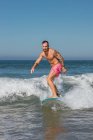 Aktive Männer in Badehosen stehen auf dem Surfbrett, während sie an einem sonnigen Sommertag im wogenden Meer im tropischen Badeort surfen — Stockfoto