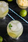Von oben kommen kalte Cocktails, bestehend aus Limettenstücken, Eiswürfeln und Minzblättern, serviert mit einer Schüssel gehackter Ananas — Stockfoto