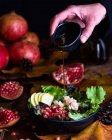 Crop anonymous chef adding olive oil in bowl with appetizing vegetarian pomegranate salad served on table with autumn leaves and cones — Stock Photo