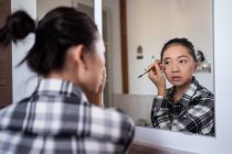 Konzentrierte charmante ethnische Frau, die Augenbrauenstift aufträgt, während sie Make-up macht und in den Spiegel schaut — Stockfoto
