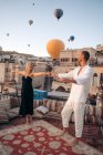 Все тело босых пар танцуют вместе на террасе на крыше против воздушных шаров, летающих в безоблачном небе, глядя друг на друга — стоковое фото
