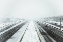 Auto che guidano su una strada asfaltata liscia coperta di neve in una cupa giornata invernale durante la nevicata a Madrid — Foto stock