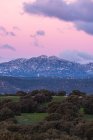 Paysage à couper le souffle d'une chaîne de montagnes rocheuses et d'une vallée avec des arbres verts sous un ciel rose au coucher du soleil avec des nuages dans le parc national de Sierra de Guadarrama en Espagne — Photo de stock
